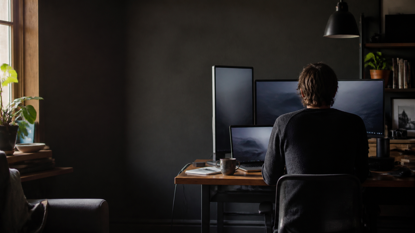 A focused person working at a warm, naturally lit multi-display desk